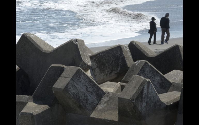 Una pareja pasea por la playa, en la que quedaron semienterrados bloques gigantes de cemento de un rompeolas tras el tsunami. EFE  /