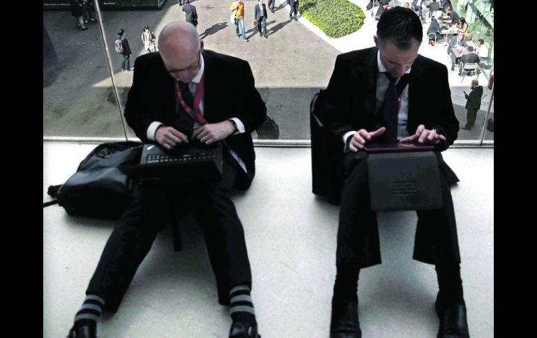 Dos ejecutivos trabajan con sus laptops en el suelo de una de las pasarelas en el Mobile World Congress. EFE /