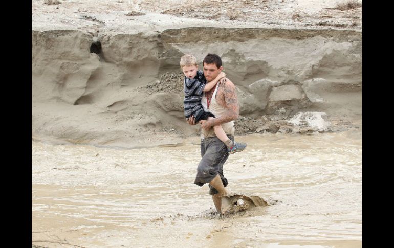 Hombre carga a un niño para atravesar una carretera, inundada por las lluvias que el metéoro causa en California. AP  J. Calderón  /