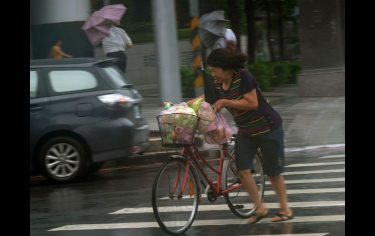 Una mujer trata de caminar con su bicicleta ante los fuertes vientos. AFP / S. Yeh
