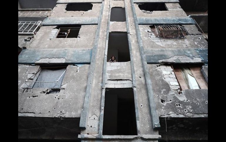 Una niña ve a través de la ventana de uno de los edificios dañados. AFP / A. Doumany