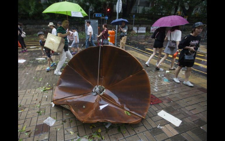 Varios viandantes pasan junto a un plato de un satélite que voló de un tejado por el paso del tifón 'Hato' en Hong Kong. EFE / A. Hofford