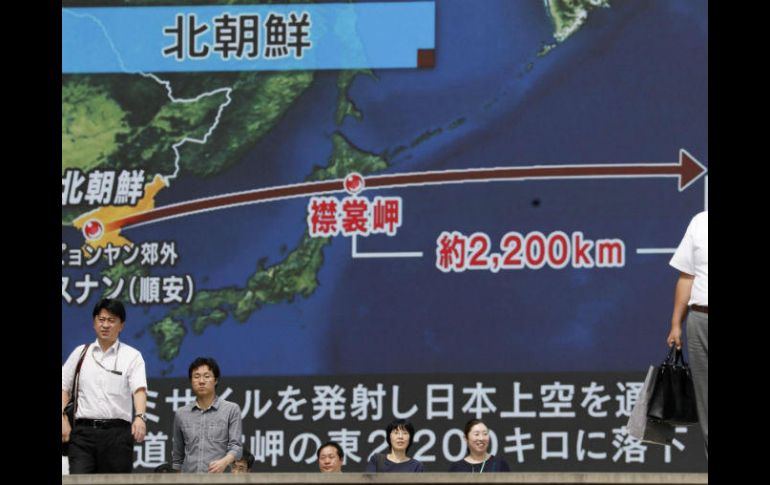 Peatones caminan bajo un monitor a gran escala que muestra el vuelo de un misil balístico norcoreano sobrevolando Japón. EFE / K. Mayama