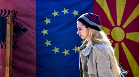Una mujer camina frente a las banderas de Albania, la Unión Europea y Macedonia del Norte. EFE/G. Licovski